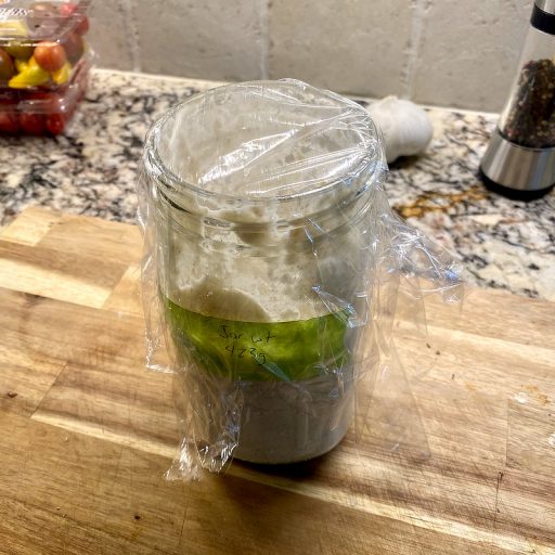 A quart mason jar half full of sourdough starter on a wooden cutting board on my counter.
