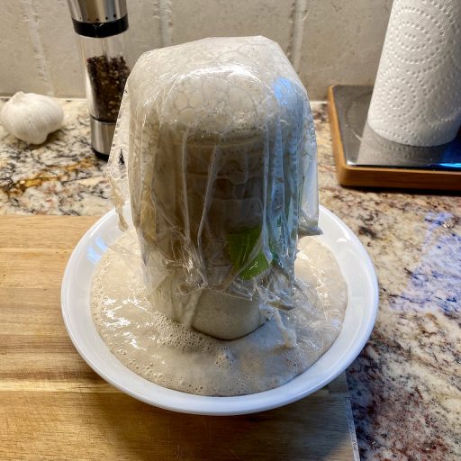 A quart mason jar of sourdough starter, with the starter overflowing into the wide, flat bowl it's sitting in.