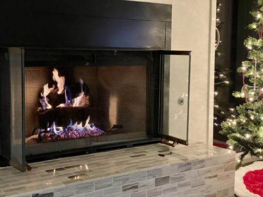 Our gas-log fireplace with a fire burning for the first time. A tile hearth and the very edge of our lit Christmas tree.