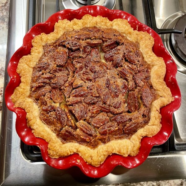 A pecan pie in a red, ruffled, ceramic pie pan.