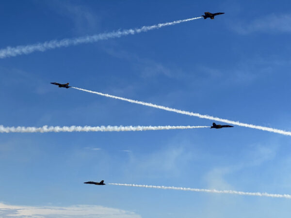 Four jets crossing the frame toward each other against a blue sky.