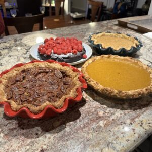 Four desserts: pecan pie, pumpkin pie, apple pie, and a chocolate tart.