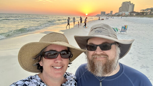 A selfie of me and Mr M in wide-brimmed hats with the beach and sunset in the background.
